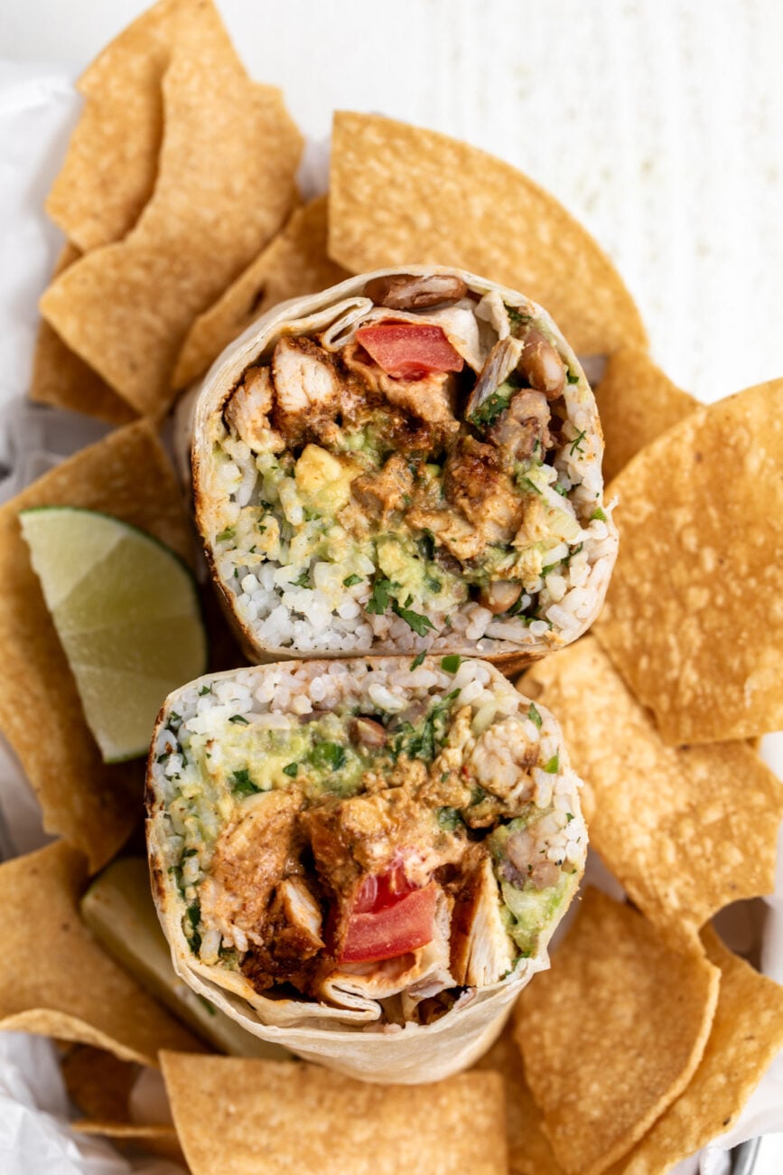 creamy chipotle chicken burrito cut in half with seasoned chicken pinto beans and rice.