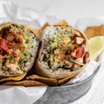 creamy chipotle chicken burrito cut in half with seasoned chicken pinto beans and rice.