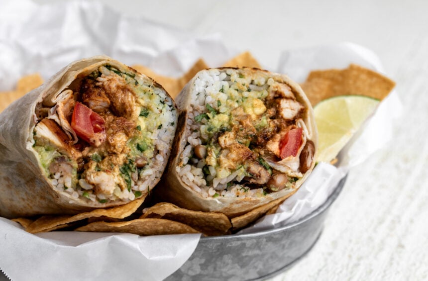 creamy chipotle chicken burrito cut in half with seasoned chicken pinto beans and rice.