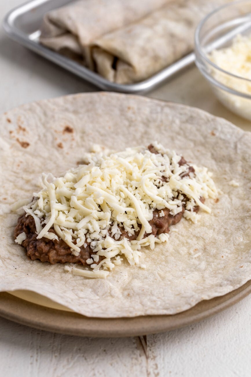 assembled bean and cheese burrito with flour tortilla topped with refried beans and monterey jack cheese.