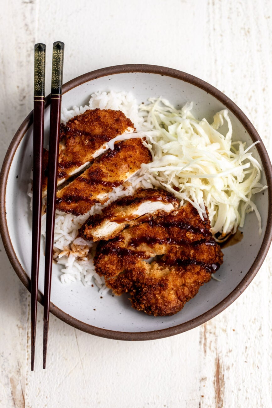 crispy chicken cutlets with rice, shredded cabbage and tonkatsu sauce.