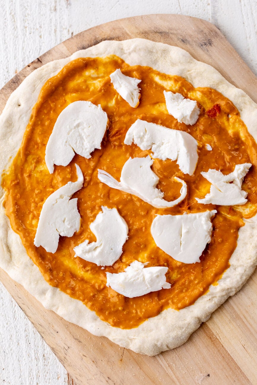 Prepared pizza dough topped with confit sungold tomato pizza with mozzarella. 
