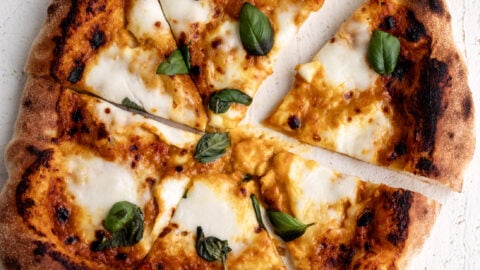 Sungold tomato pizza with mozzarella and basil cut into pieces.