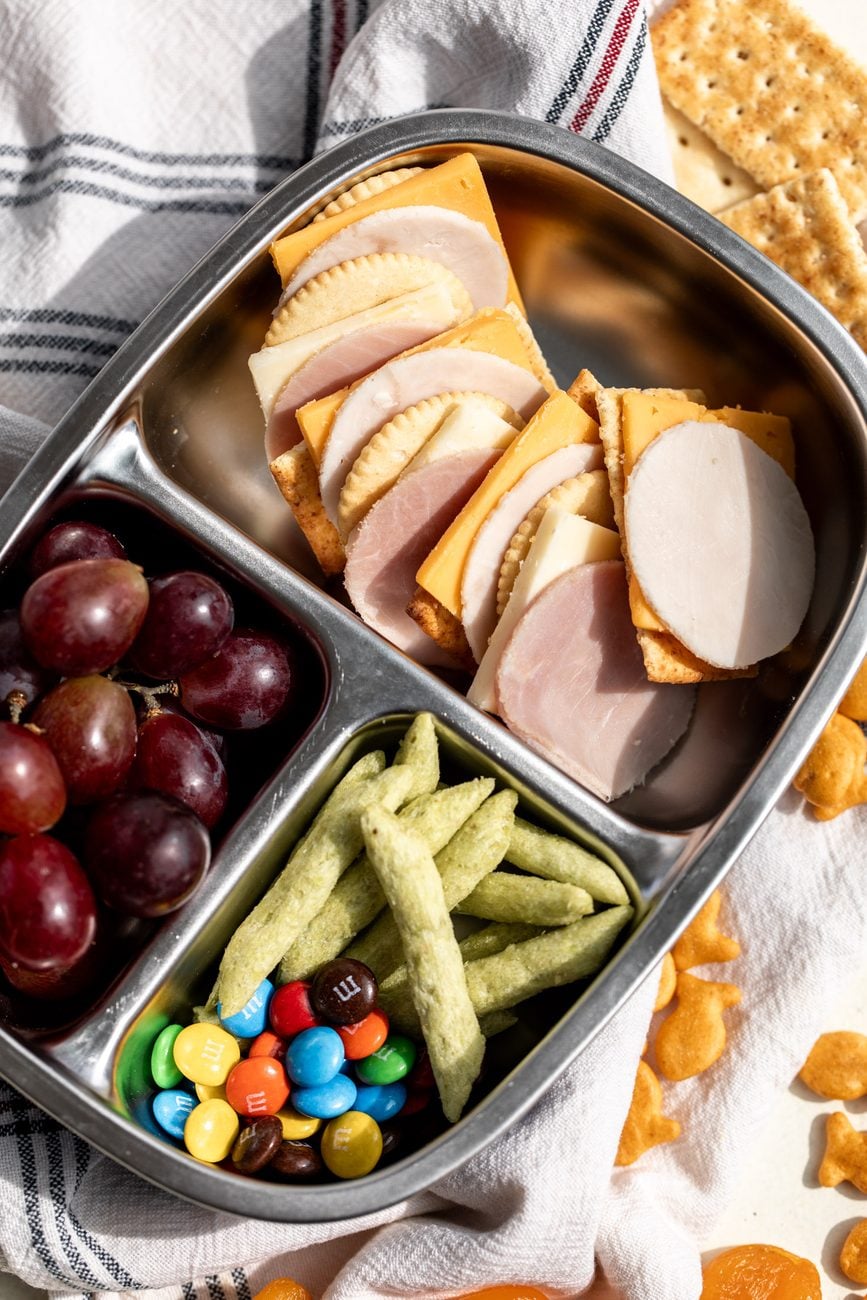 homemade lunchables in bento box with other snacks like grapes and crispy snap peas.