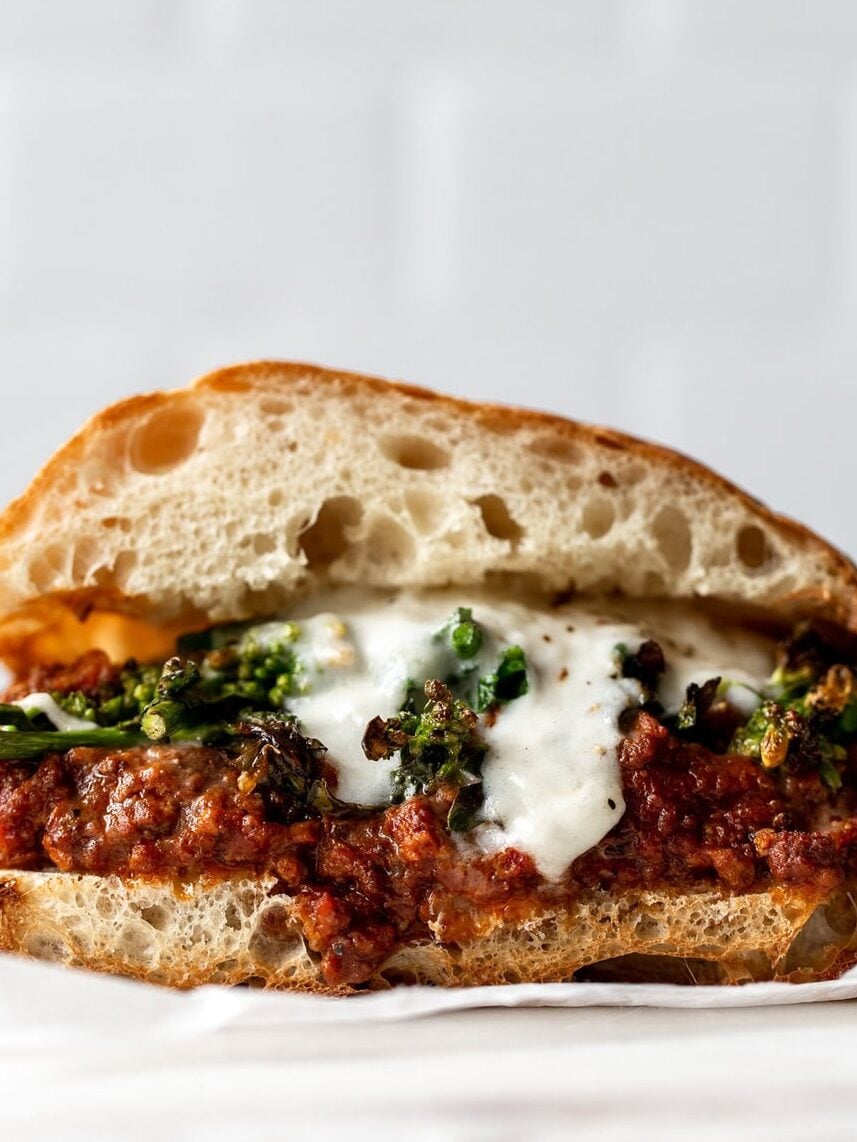 bolognese, rapini and burrata layered onto a ciabatta split bun on a white marble.